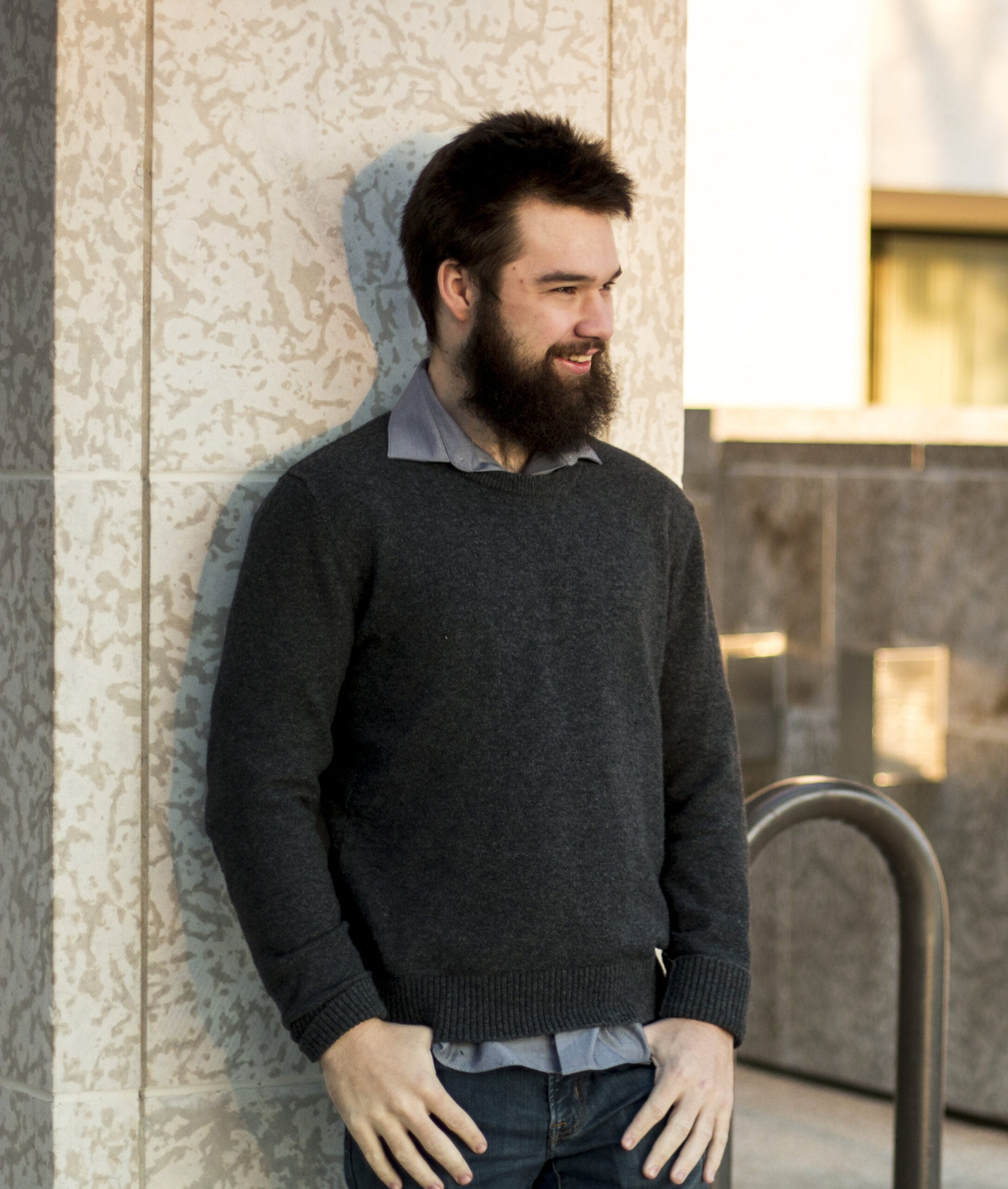 John, a white man with a beard, is standing in front of a column with his hands in his pockets.