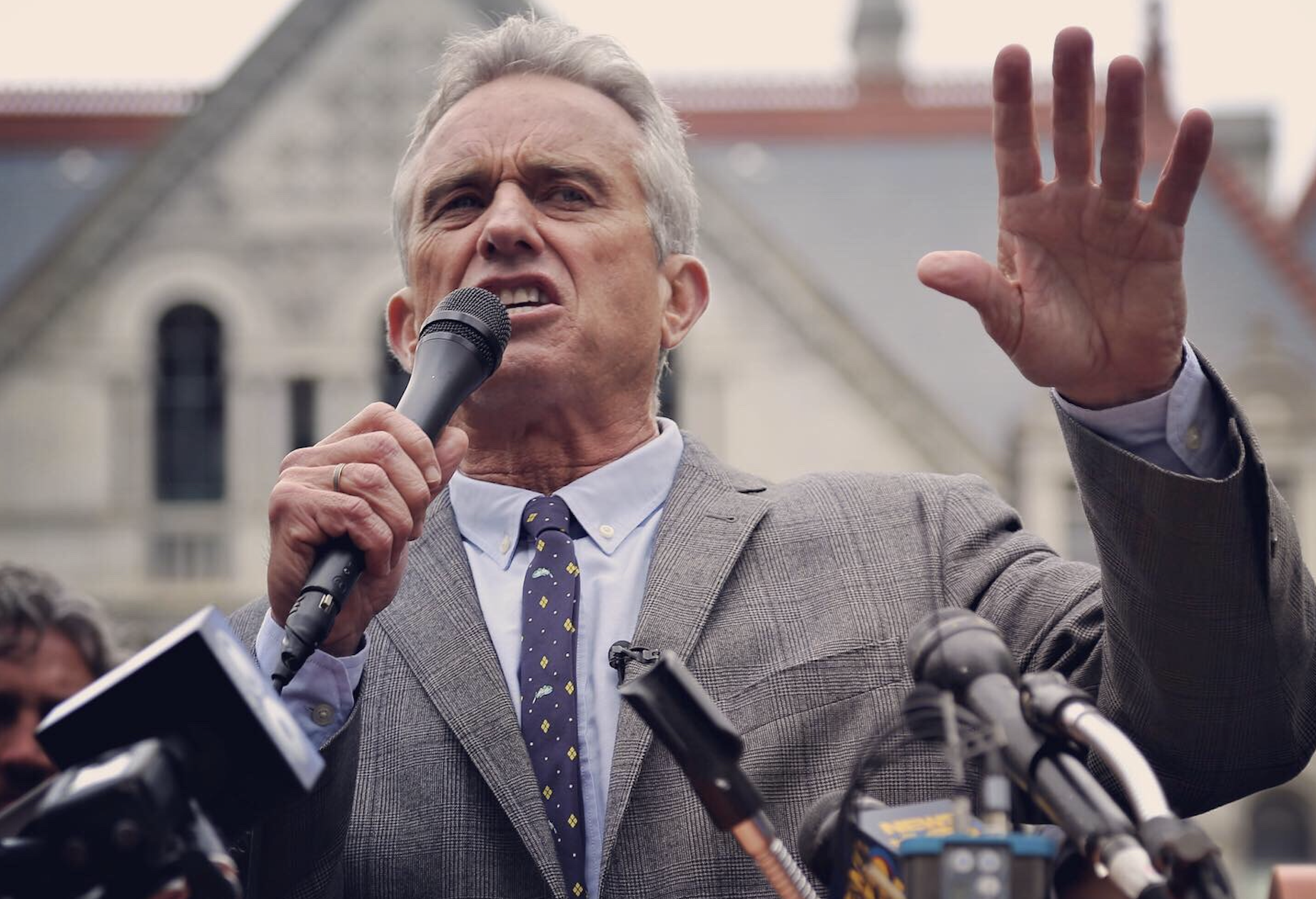 Robert F. Kennedy Jr. standing at a podium, holding a microphone in front of a church