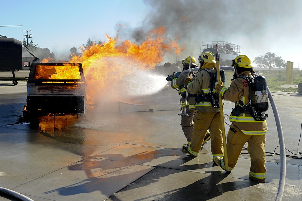 A student firefighter team, dressed in full gear, puts out a dumpster fire during a training exercise