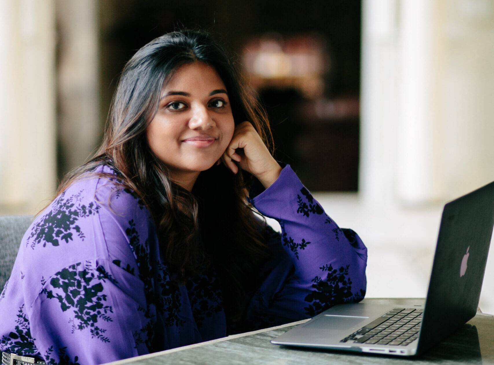 Journalist Sonali Gupta wearing a purple shirt with black pint, seated at a table with a laptop open in front of her