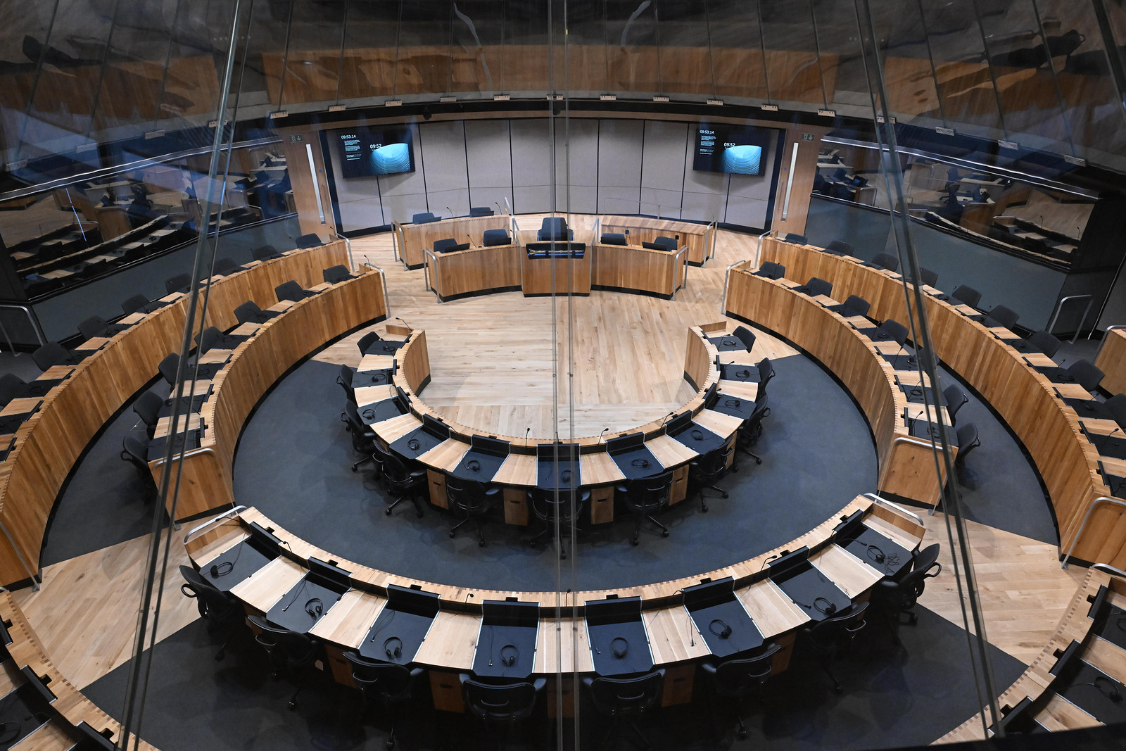 An image of the Welsh Parliament, multiple circles of seats with wood paneling.