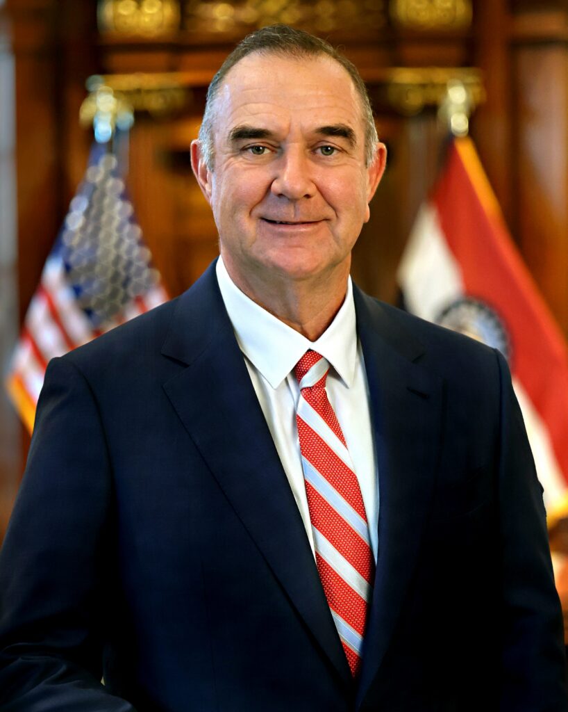 Missouri Gov. Mike Kehoe wears a dark suit, white shirt and red and white stiped tie