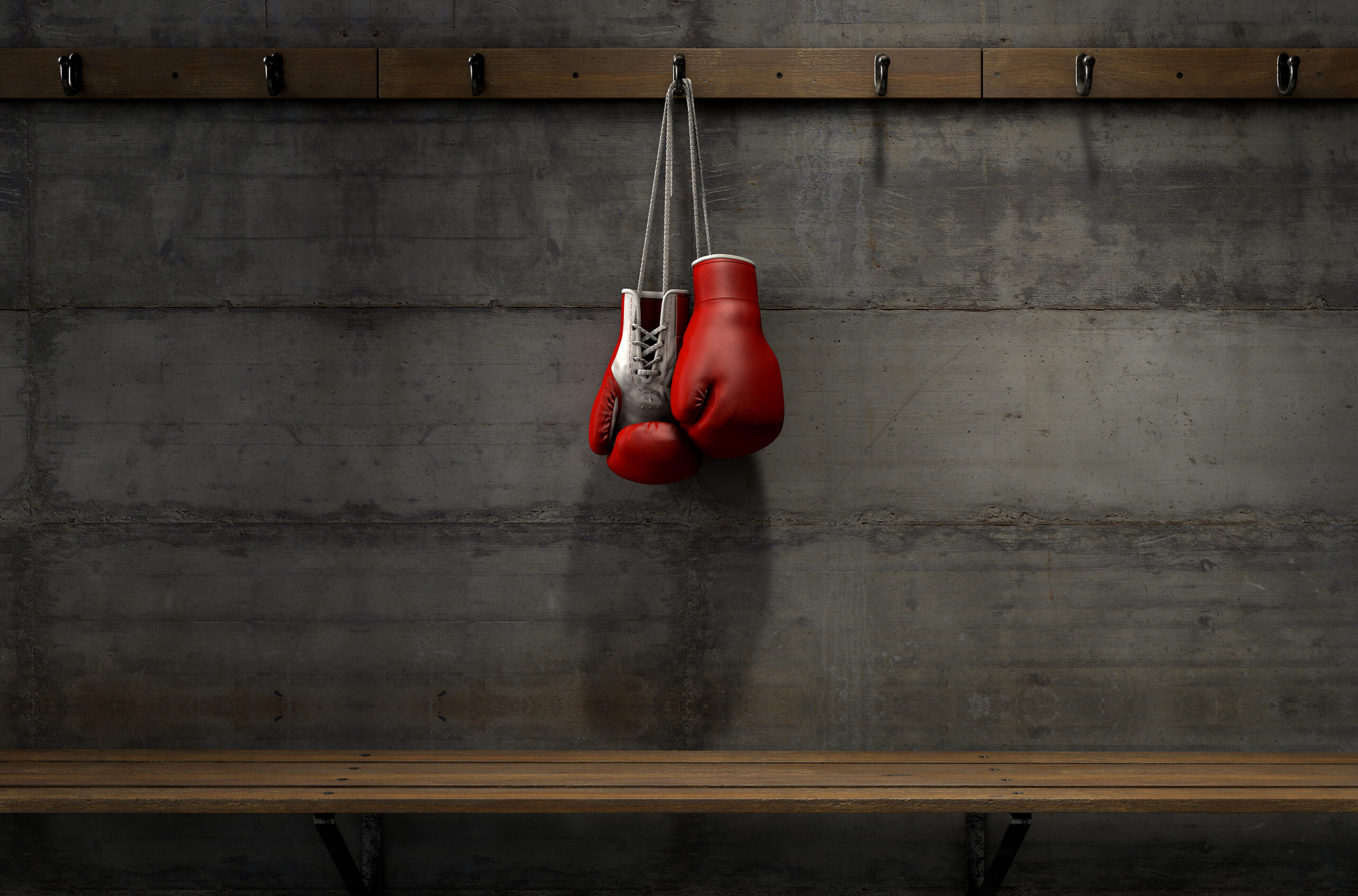 Spotlit boxing gloves hanging on a hanger above an empty wooden bench in a locker change room.