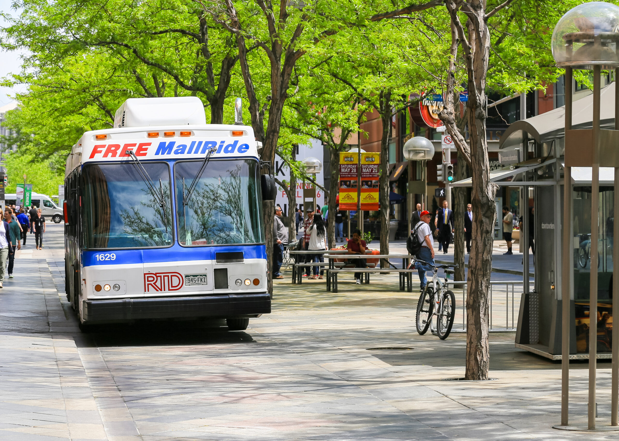 A bus in the 16th street mall in downtown Denver offering free mall ride. People are doing shopping or dining in the several shops and cafes.