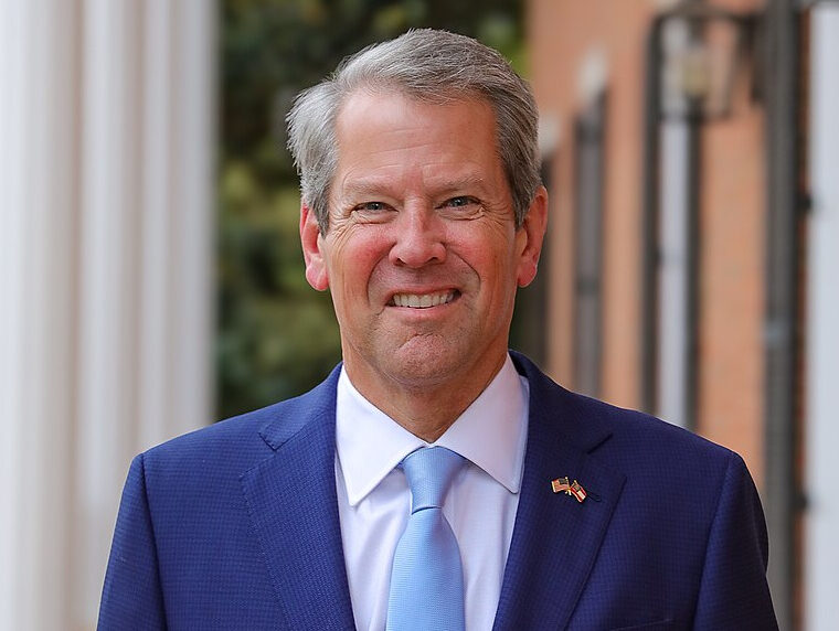 Brian Kemp, governor of Georgia, in a blue vest and blue tie. He is smiling to the camera