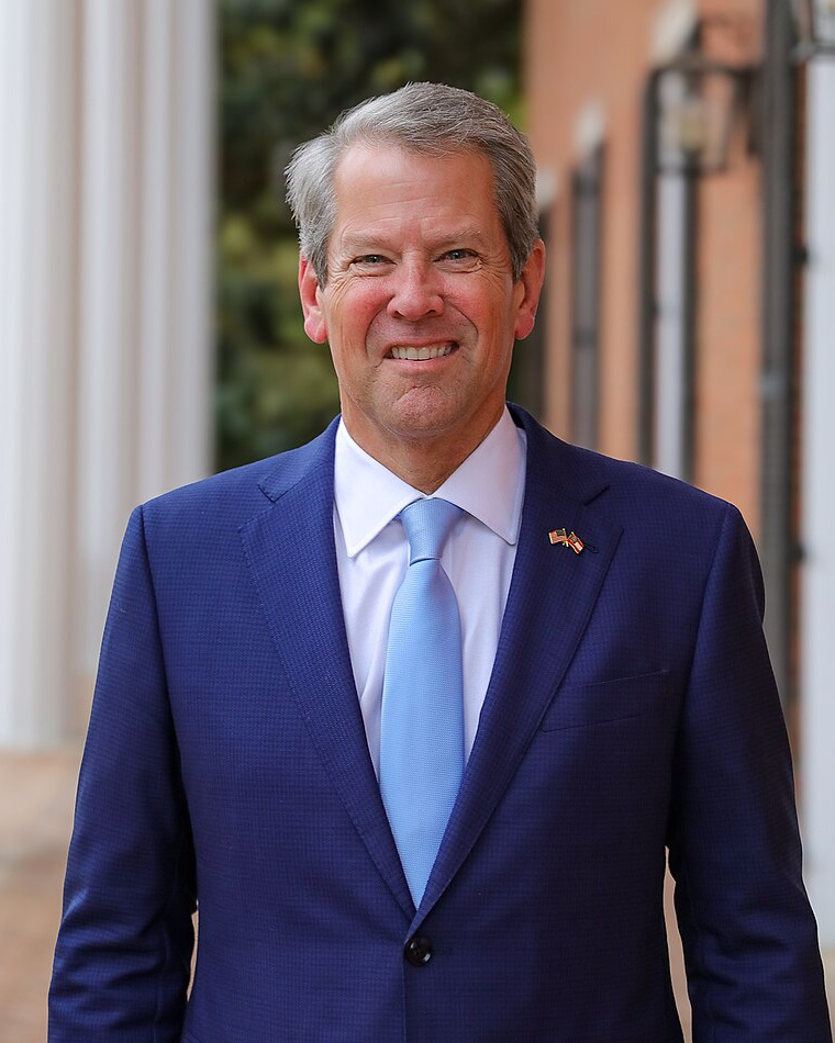 Brian Kemp, governor of Georgia, in a blue vest and blue tie. He is smiling to the camera