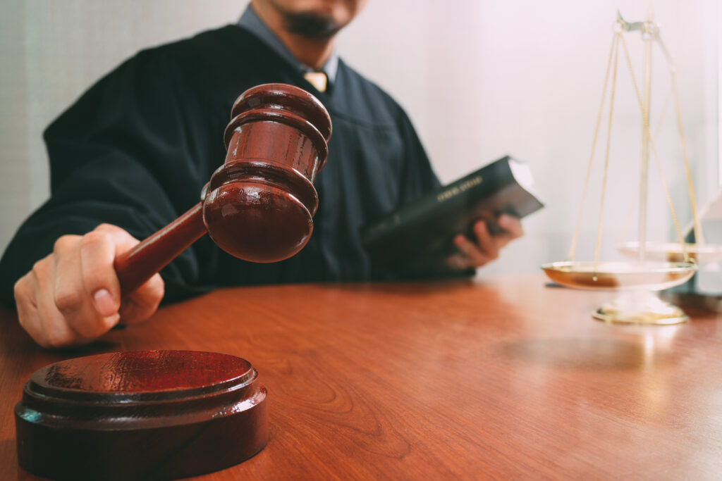 Male judge in a courtroom with the gavel and working with holy book and brass scale on wood table.