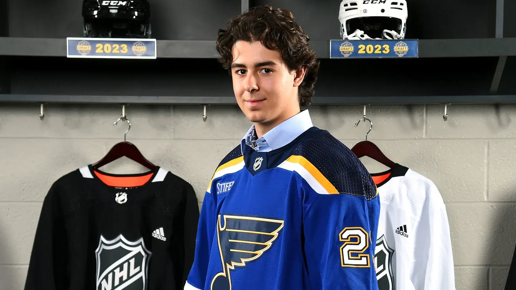 Image of Mathew Mayich, a hockey player, in front of his locker in a blue St. Louis Blues jersey